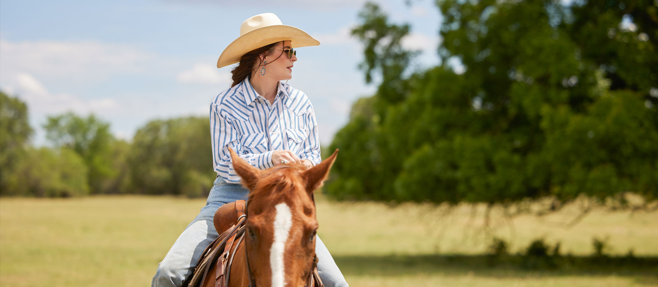 A cowgirl on her horse in an open field on a sunny day.